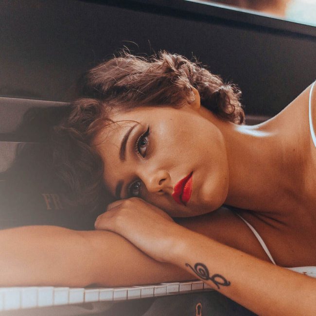 Femme allongée sur un piano, le regard fatigué, symbolisant la lassitude et la douleur des répétitions inconscientes en psychanalyse.